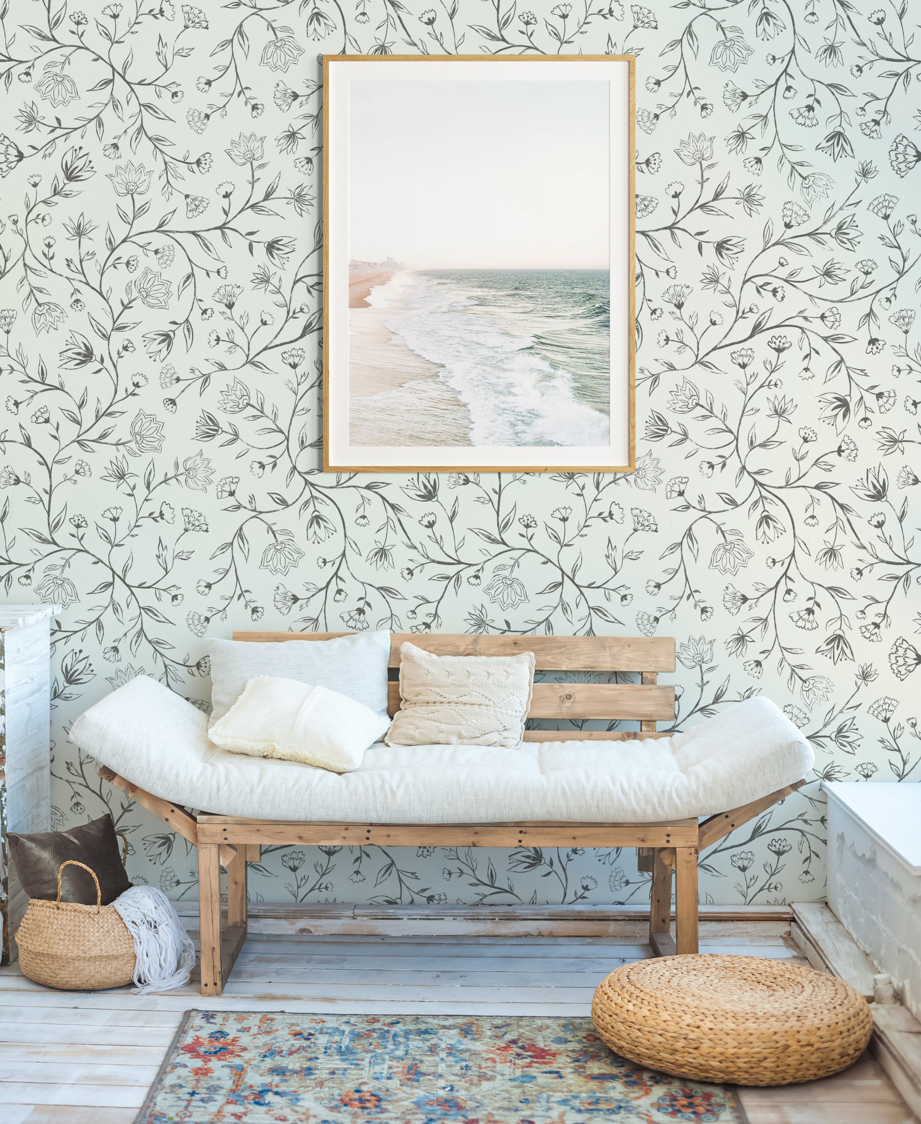 Wooden bench with white cushions against a floral wallpaper wall with a framed picture.